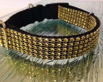 Puede incluir: Un collar de perro negro con diamantes de imitación dorados. El collar está hecho de una correa de nylon negra con una hebilla y un anillo en D dorados.