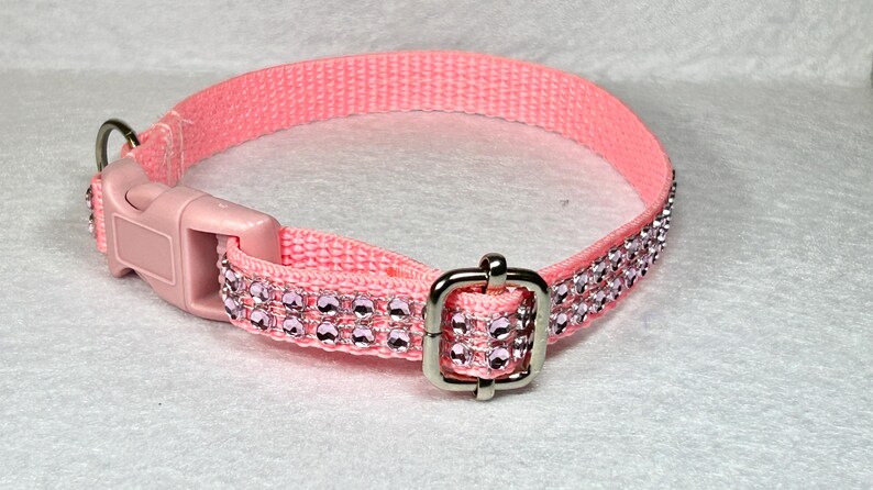 May include: A pink nylon dog collar with a silver buckle and two rows of clear pink rhinestones.