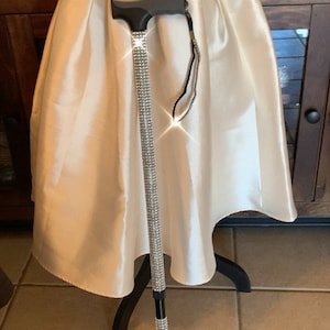 Puede incluir: Un bastón de caminar negro y plateado con un diseño de diamante. El bastón tiene un mango negro y una punta negra. El bastón está de pie sobre un suelo de baldosas.