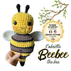 Op de afbeelding: Een gehaakte bijenknuffel in geel, bruin en zwart, met witte vleugels. De bij heeft grote zwarte ogen, roze wangen en zwarte antennes. De tekst "l'abeille Beebee the bee" staat eronder.