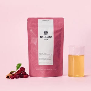 May include: A pink tea bag labeled "OSULLOC Berry Garden Green Tea" with a glass of tea and a small pile of berries and a cinnamon stick. The tea bag has a white vertical stripe with the brand name and logo. The glass contains a light amber liquid.