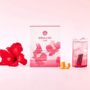 Peut inclure: Une boîte de thé froid OSULLOC Sweet Hibiscus, une fleur d'hibiscus rouge et un verre de thé glacé. La boîte est blanche et rose avec du texte coréen et un motif floral. Une peau d'orange est à côté du verre.
