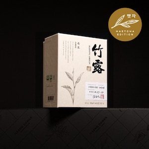 May include: A beige box of tea with the text "竹露" in black. The box has a drawing of a tea plant and the words "HADONG ORIGIN" and "JUKRO". A gold circle with the text "HAETCHA EDITION" is in the upper right corner.
