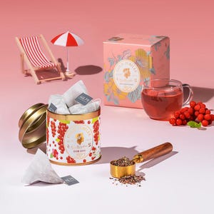 May include: A still-life image featuring a tea set with a pink background. A decorative tin with red berry illustrations and the text "GOLD JUBILEE" is open, revealing tea bags. A box with floral designs and a teacup filled with tea are also present.