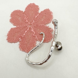 May include: Silver ear cuff with a textured, organic shape. The cuff is open and has a small post for attaching to the ear.