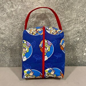 May include: A blue and red zippered pouch with a repeating pattern of Toy Story characters, including Woody and Buzz Lightyear. The pouch has a red handle.