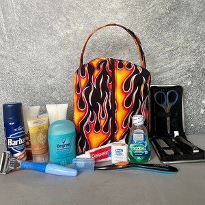 May include: A black toiletry bag with a flame pattern in orange and yellow. The bag is open and contains various toiletries, including a razor, shaving cream, deodorant, body wash, toothpaste, mouthwash, and a nail clipper set.