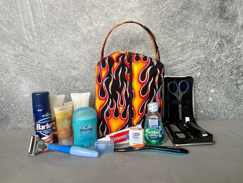 May include: A black toiletry bag with a flame pattern in orange and yellow. The bag is open and contains various toiletries, including a razor, shaving cream, deodorant, body wash, toothpaste, mouthwash, and a nail clipper set.