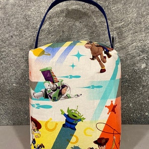 May include: A colorful fabric doorstop with a blue handle. The fabric features a pattern of characters from the Toy Story movie franchise, including Woody, Buzz Lightyear, and the alien.