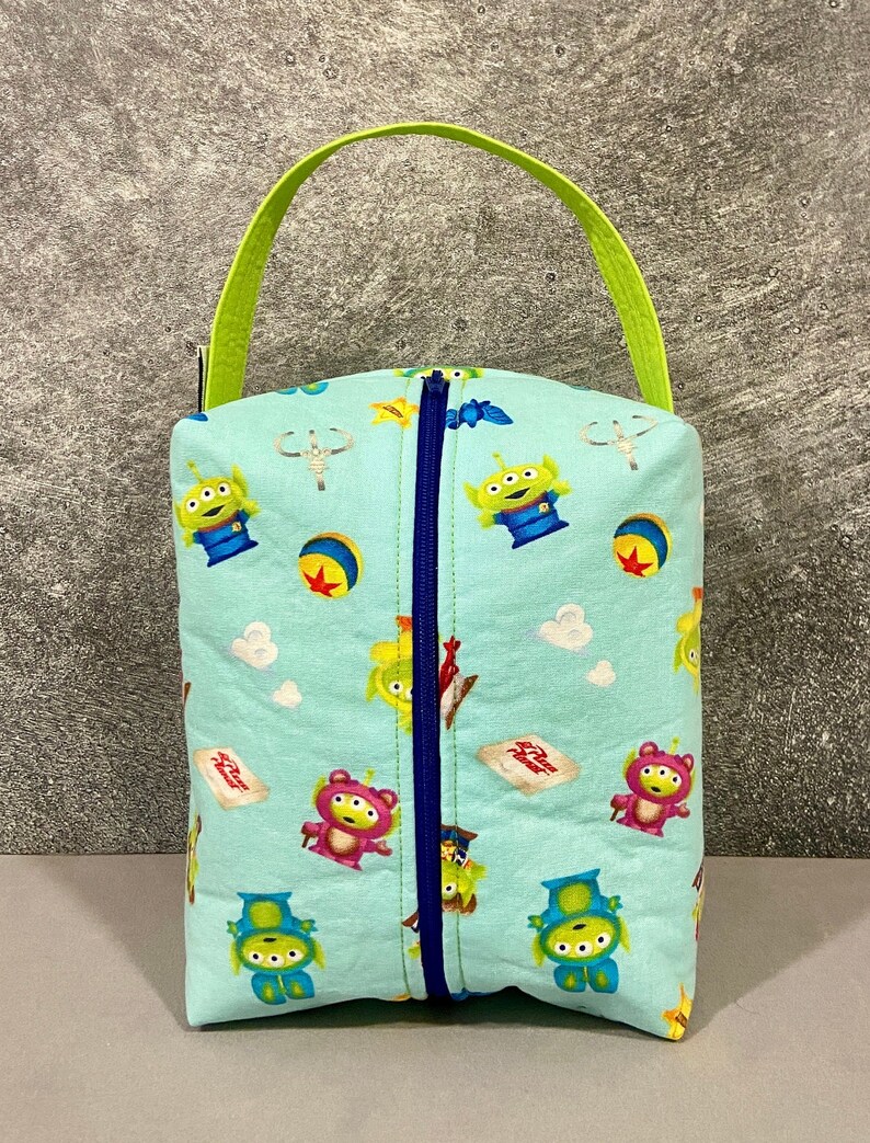 May include: A light blue zippered pouch with a green handle. The pouch is decorated with a repeating pattern of alien characters from the Toy Story franchise.