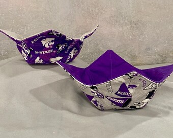 May include: Two purple and white fabric bowl cozies with a K-State Wildcats design. The cozies are folded and ready to use.