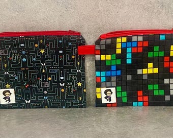 May include: Two black zippered pouches with red zippers. One pouch has a pixelated design with colorful squares. The other pouch has a black and white design with a maze pattern and a small cartoon figure.