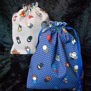May include: Two fabric drawstring bags with polka dot patterns. One bag is white with red polka dots and features cartoon characters. The other bag is blue with white polka dots and features cartoon characters.