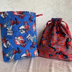 May include: Two drawstring bags with a Spiderman theme. One bag is blue with red and black Spiderman images and the text "Ultimate Spider-Man". The other bag is red with black Spiderman images and the text "Not So Scary But Pretty Darn Cool".