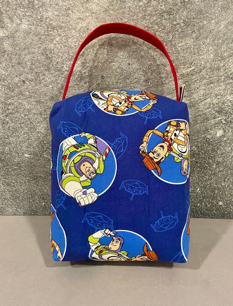 May include: A blue fabric tote bag with a red handle. The bag features a repeating pattern of Toy Story characters, including Woody and Buzz Lightyear.
