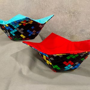 May include: Two fabric bowls with a black and colorful geometric pattern. One bowl is lined with blue fabric and the other with red fabric.