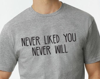 May include: A heather grey t-shirt with the text "NEVER LIKED YOU NEVER WILL" printed in black.