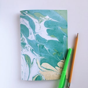 May include: A notebook with a marbled cover in shades of teal, white, and gold. The cover has a swirling pattern reminiscent of water.