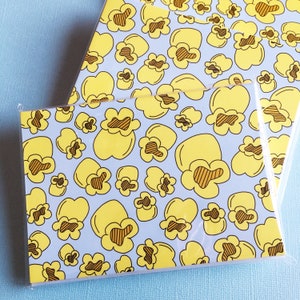 May include: A set of two note cards with a light blue background and a repeating pattern of yellow popcorn. The popcorn is outlined in black and has brown stripes.