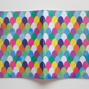 Puede incluir: Una tarjeta doblada con un patr&oacute;n colorido de c&iacute;rculos superpuestos en tonos de azul, verde, amarillo, naranja, rosa y morado. Los c&iacute;rculos est&aacute;n dispuestos en un patr&oacute;n repetitivo, creando un dise&ntilde;o visualmente atractivo.