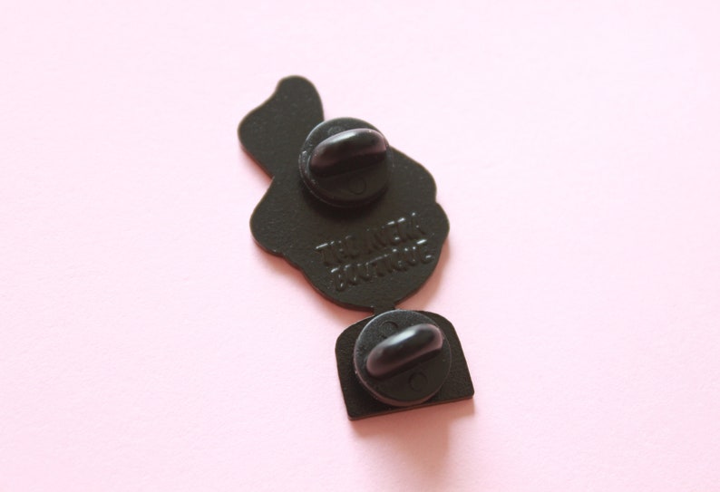 May include: Black enamel pin featuring a cartoon image of a person holding a microphone. The pin has two metal clasps on the back and the text "The Neck Don't Truss" printed on the back.