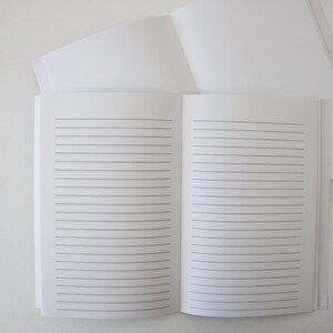 May include: A white lined notebook with a blank cover. The notebook is open to reveal lined pages.