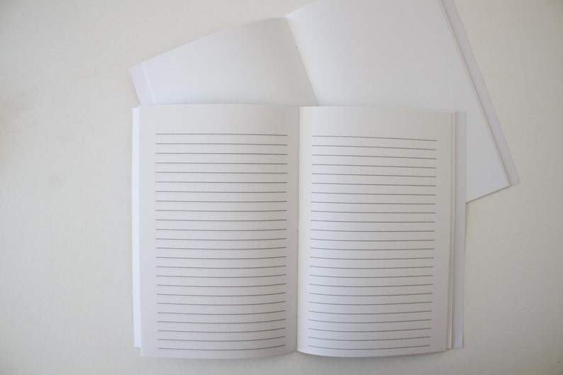 May include: A white lined notebook with a blank cover. The notebook is open to reveal lined pages.