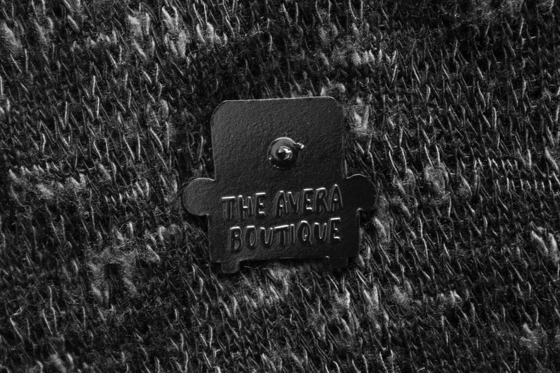 Peut inclure: &Eacute;pinglette en m&eacute;tal noir en forme de fauteuil avec le texte "THE AVERA BOUTIQUE" dessus.