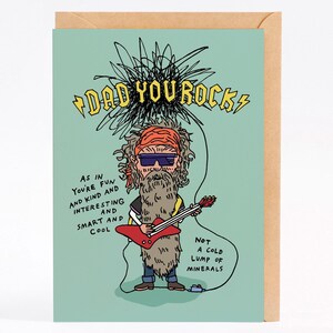 Op de afbeelding: Een kaart met een cartoonillustratie van een man met een lange baard en een zonnebril die een rode elektrische gitaar bespeelt. De tekst op de kaart luidt "DAD YOU ROCK" en "AS IN YOU'RE FUN AND KIND AND INTERESTING AND SMART AND COOL NOT A COLD LUMP OF MINERALS".