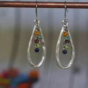 May include: Silver teardrop earrings with colorful beads dangling from the bottom.