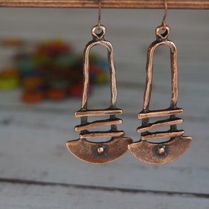 May include: A pair of long, copper earrings with a geometric design. The earrings are made of thick, textured copper wire and have a simple, modern look.