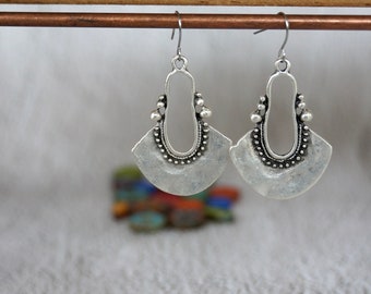 May include: A pair of silver earrings with a fan-shaped design and a beaded border. The earrings have a hook closure.