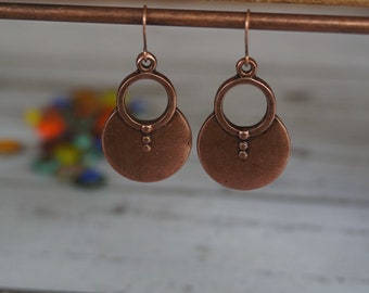 Könnte beinhalten: Ein Paar kupferne Ohrringe mit einem Kreisdesign und drei kleinen Punkten an jedem Ohrring.