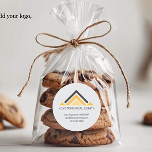 Pu&ograve; includere: Un sacchetto trasparente di cellophane legato con spago, pieno di biscotti con gocce di cioccolato. Un adesivo rotondo con il testo "KEYSTONE REAL ESTATE" &egrave; sul sacchetto. Il testo "You can add your logo, if desired" &egrave; in alto.