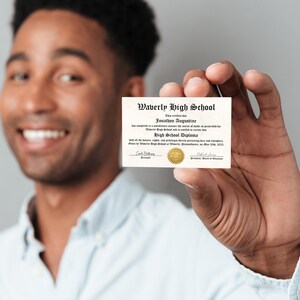 May include: A person holds up a high school diploma from Waverly High School for Jonathan Augustine. The diploma is dated May 18, 2023.