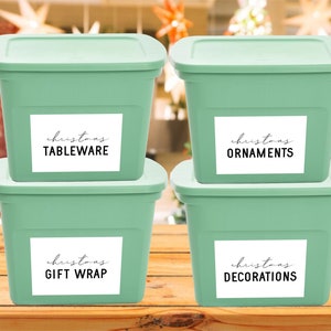 May include: Four green plastic storage bins with white labels. The labels have black text that reads "christmas TABLEWARE", "christmas ORNAMENTS", "christmas GIFT WRAP", and "christmas DECORATIONS".