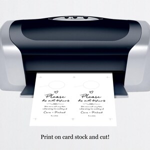 May include: Two white cards with black text that reads "Please do not disturb" with a heart symbol above the text. The text also includes the names "Cara & Michael" and the date "8.5.2023". The cards are being printed on a black and silver printer. The text at the bottom of the image reads "Print on card stock and cut!"