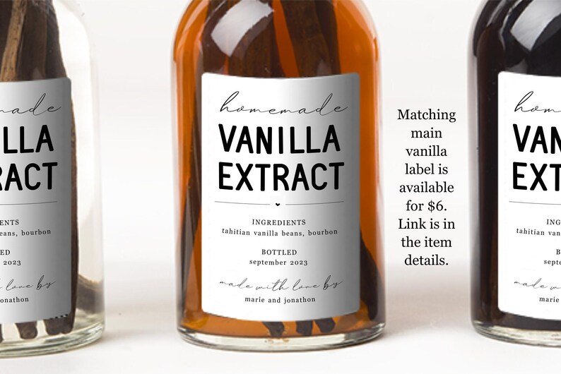 May include: A clear glass bottle filled with amber liquid and dark vanilla beans, featuring a white rectangular label with black text that reads Homemade Vanilla Extract, Ingredients Tahitian vanilla beans, bourbon, Bottled September 2023, made with love by marie and jonathon.