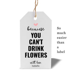 Könnte beinhalten: Weißer Geschenkanhänger mit einem rosa Herzen und schwarzem Text, der "because you can't drink flowers" lautet, mit den Worten "with love Isabella" unten. Der Anhänger hängt an einer Schnur.