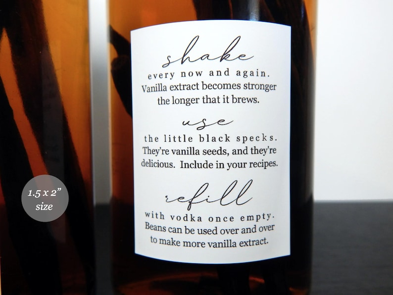 May include: A white rectangular label on an amber glass bottle containing vanilla beans. The label features black text: shake every now and again, use the little black specks, and refill with vodka once empty. A small circular icon states 3.8 x 5.1 cm size.