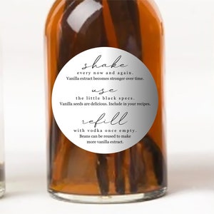 May include: Three glass bottles with silver labels containing vanilla extract. The labels have instructions for shaking, using, and refilling the bottles. The text on the labels reads: "shake every now and again. Vanilla extract becomes stronger over time. use the little black specs. Vanilla seeds are delicious. Include in your recipes. refill with vodka once empty. Beans can be reused to make more vanilla extract."