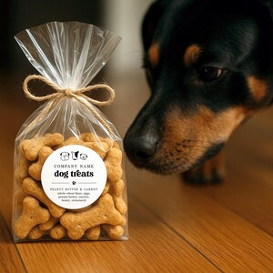 May include: A clear cellophane bag tied with twine, filled with bone-shaped dog treats. The label reads "dog treats" and lists ingredients. A black and brown dog is in the background, looking at the treats.