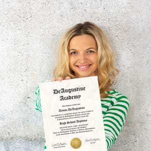 K&ouml;nnte beinhalten: Eine Frau h&auml;lt ein High School Diploma der DeAugustine Academy. Das Diplom ist cremefarben mit schwarzem Text und einem goldenen Siegel. Die Frau tr&auml;gt ein gr&uuml;n-wei&szlig; gestreiftes Hemd.