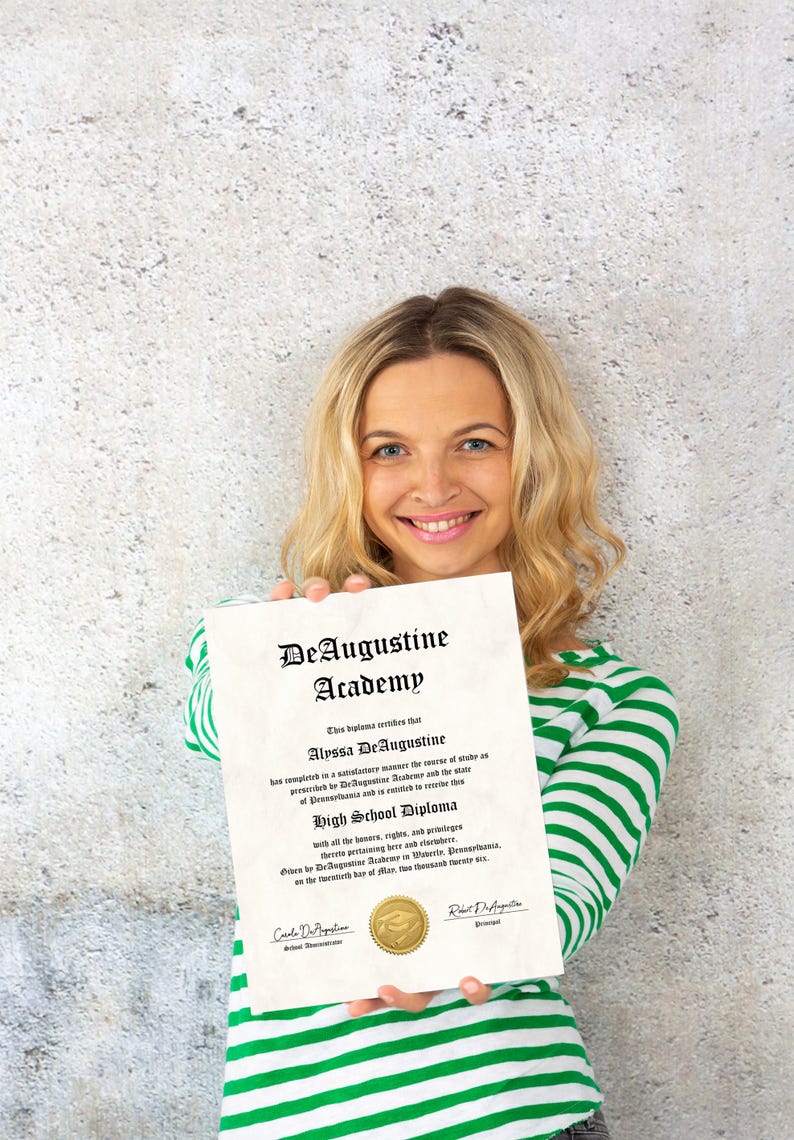 K&ouml;nnte beinhalten: Eine Frau h&auml;lt ein High School Diploma der DeAugustine Academy. Das Diplom ist cremefarben mit schwarzem Text und einem goldenen Siegel. Die Frau tr&auml;gt ein gr&uuml;n-wei&szlig; gestreiftes Hemd.