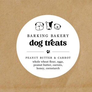 May include: A white circular label on a brown background. The label reads "BARKING BAKERY dog treats" with dog illustrations. Below, it lists ingredients: peanut butter & carrot, whole wheat flour, eggs, peanut butter, carrots, honey, and cornstarch.