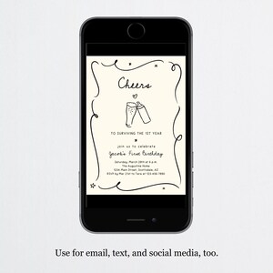 May include: A smartphone screen shows a cream-coloured invitation with black text and illustrations. The invitation says "Cheers" above two toasting glasses, with details for a first birthday celebration. The phone is black, and the background is white.
