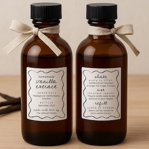 May include: Two brown glass bottles of homemade vanilla extract with black caps and cream-colored bows. Each bottle has a white label with text detailing ingredients, instructions, and bottling information. Vanilla beans are visible.