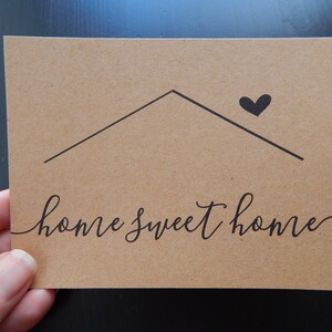 May include: A brown card with the text "home sweet home" written in black cursive script. A simple black house shape with a heart on top is above the text.