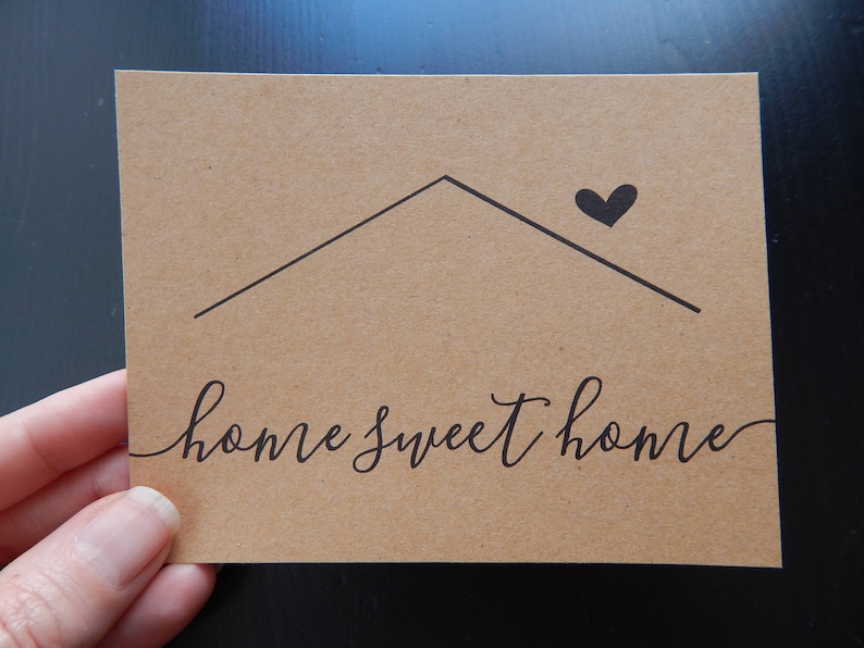 May include: A brown card with the text "home sweet home" written in black cursive script. A simple black house shape with a heart on top is above the text.