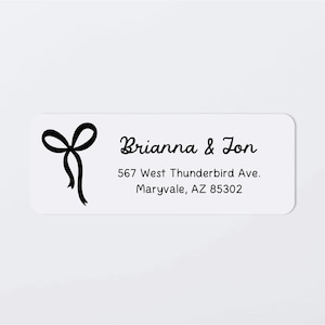 May include: White rectangular label with rounded corners. A black bow graphic is on the left. The text "Brianna & Jon" is in a script font, with the address "567 West Thunderbird Ave. Maryvale, AZ 85302" below.